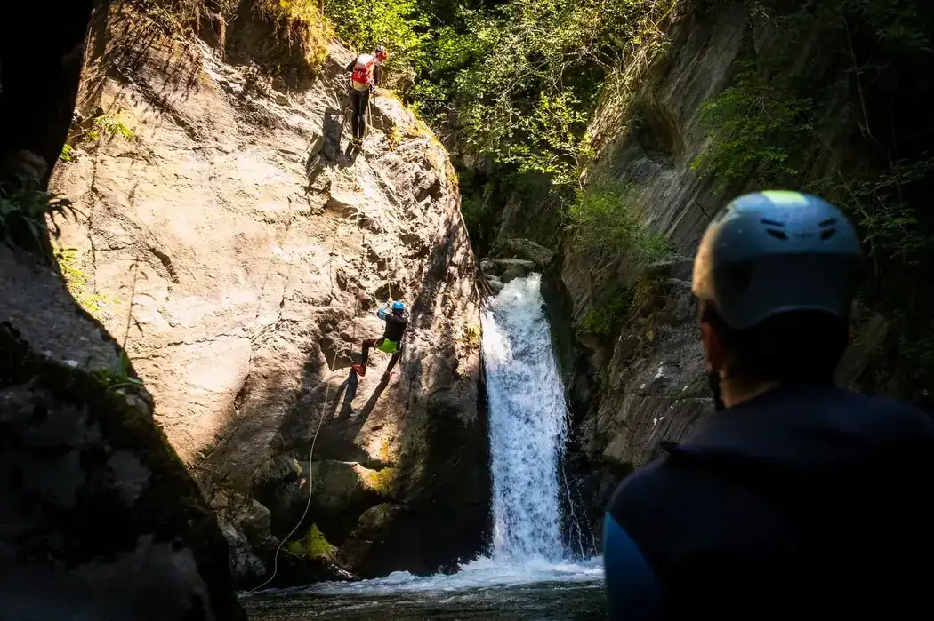 Guía de barranquismo descendiendo en rápel una pared rocosa en un cañón de Andorra, grupo observando abajo