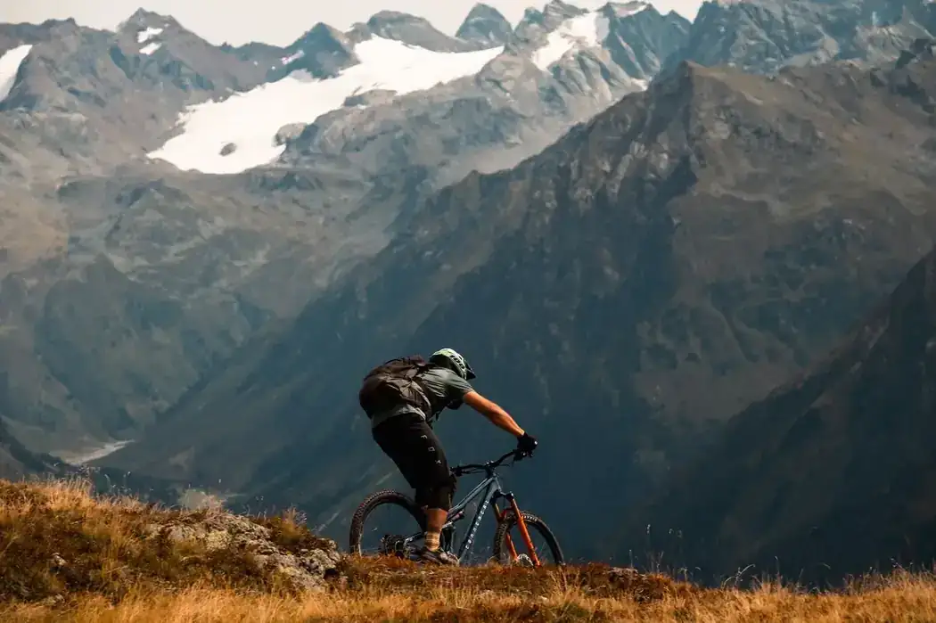 Ciclista de montaña descendiendo un sendero alpino con picos nevados de fondo