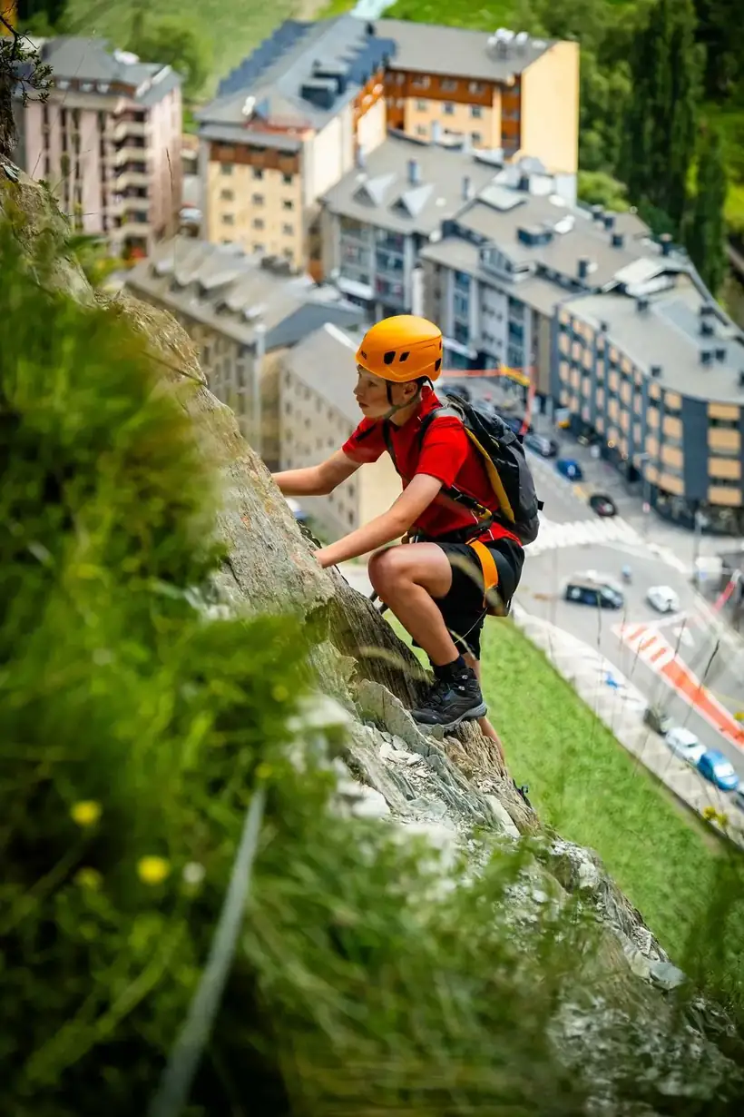 Chico escalando una vía ferrata con la ciudad de Andorra la Vella abajo