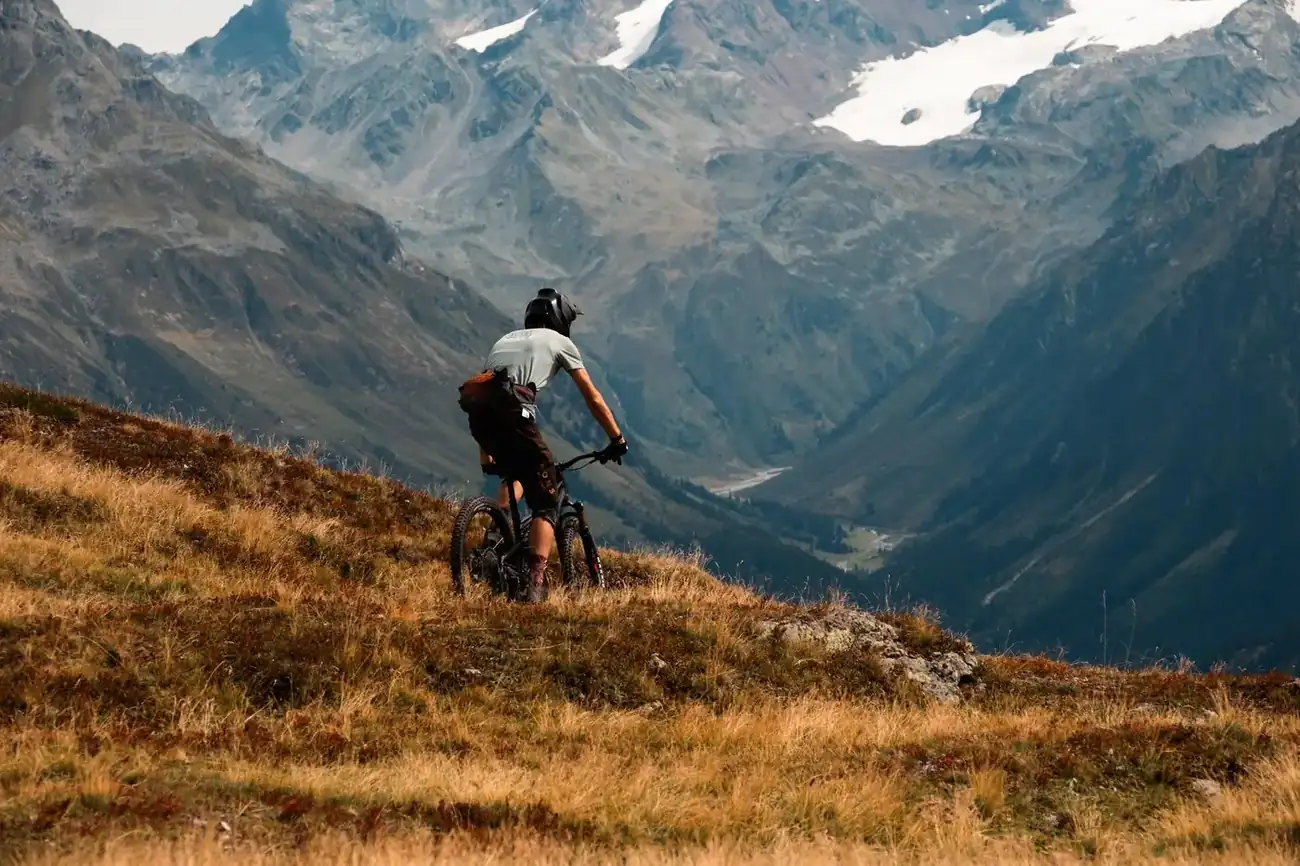 Ciclista de montaña contemplando un valle alpino desde una cresta montañosa